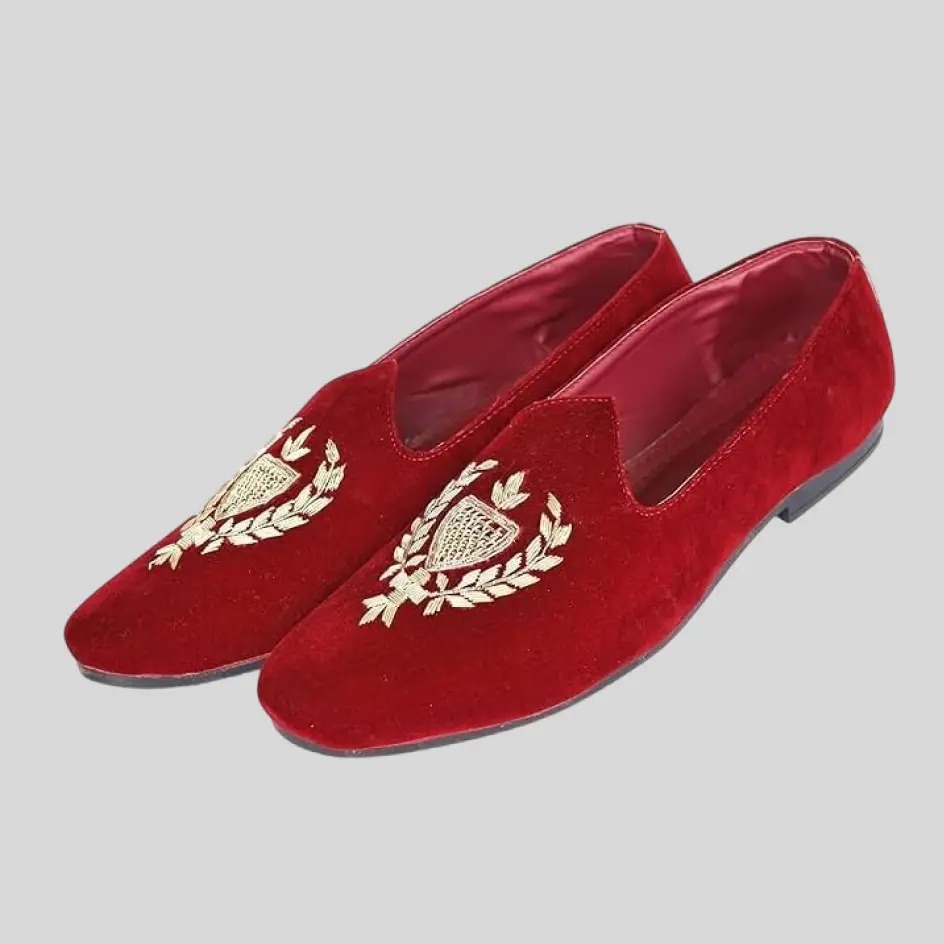 A close-up of velvet slippers with intricate embroidery, showcasing finely stitched patterns or monograms on the soft fabric.