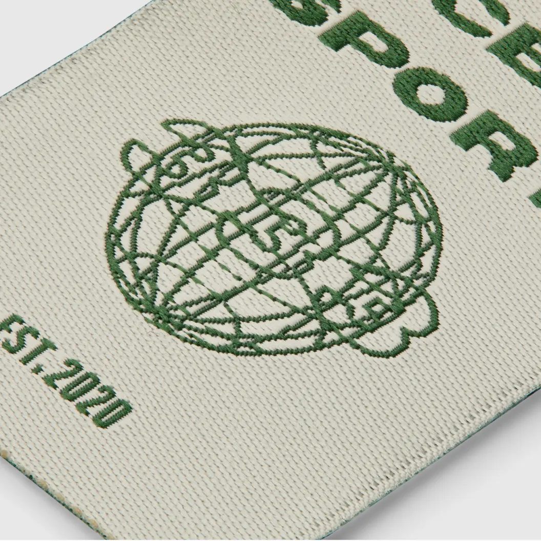 Woven patch with green text and globe design on white background.