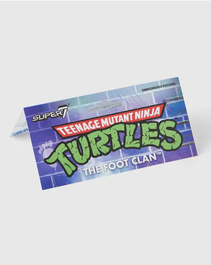 Colorful backer card with the Teenage Mutant Ninja Turtles logo and “The Foot Clan” branding in vibrant green and purple colors