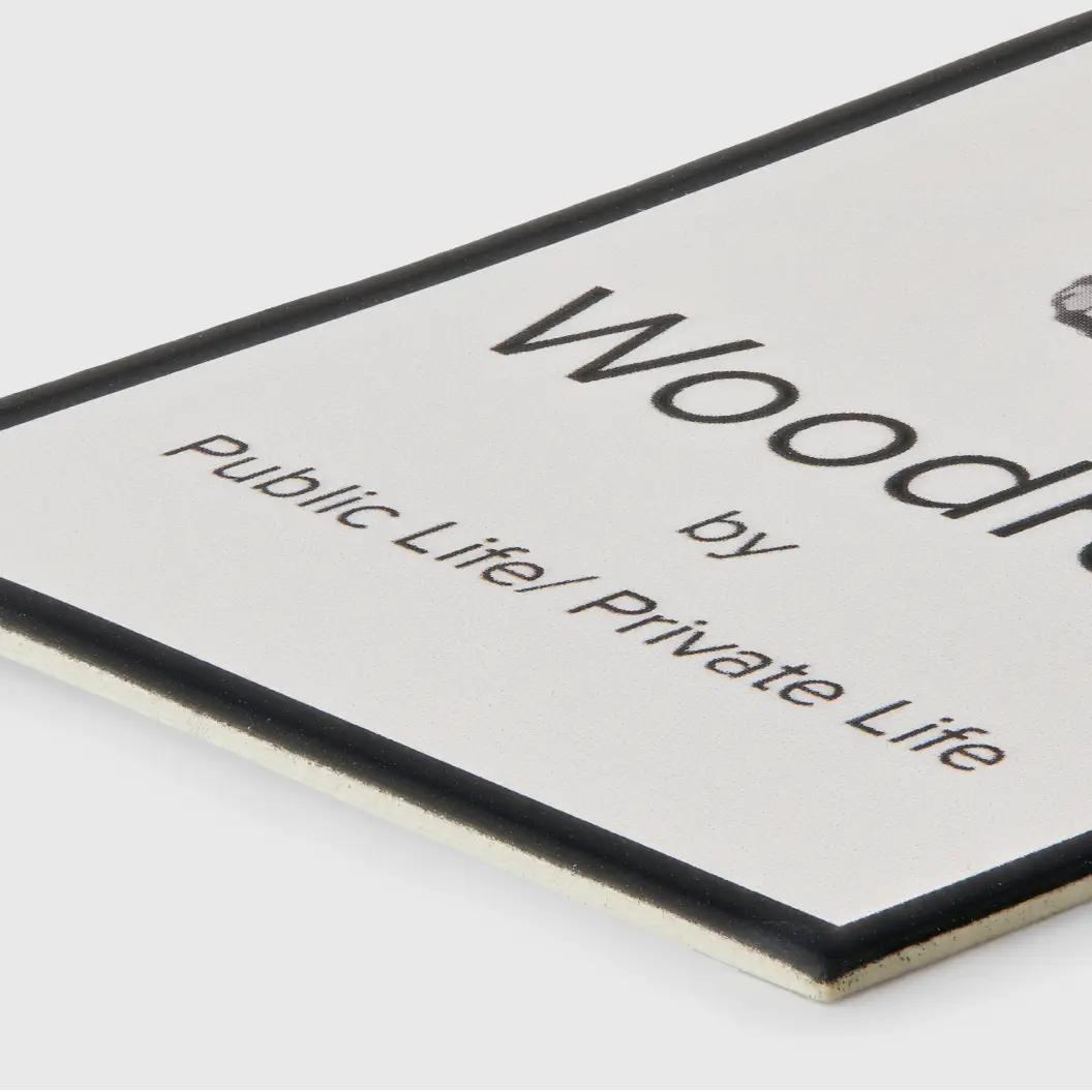 Rectangular black and white label with a minimalist design, featuring the word “Woodrich” and a tagline.