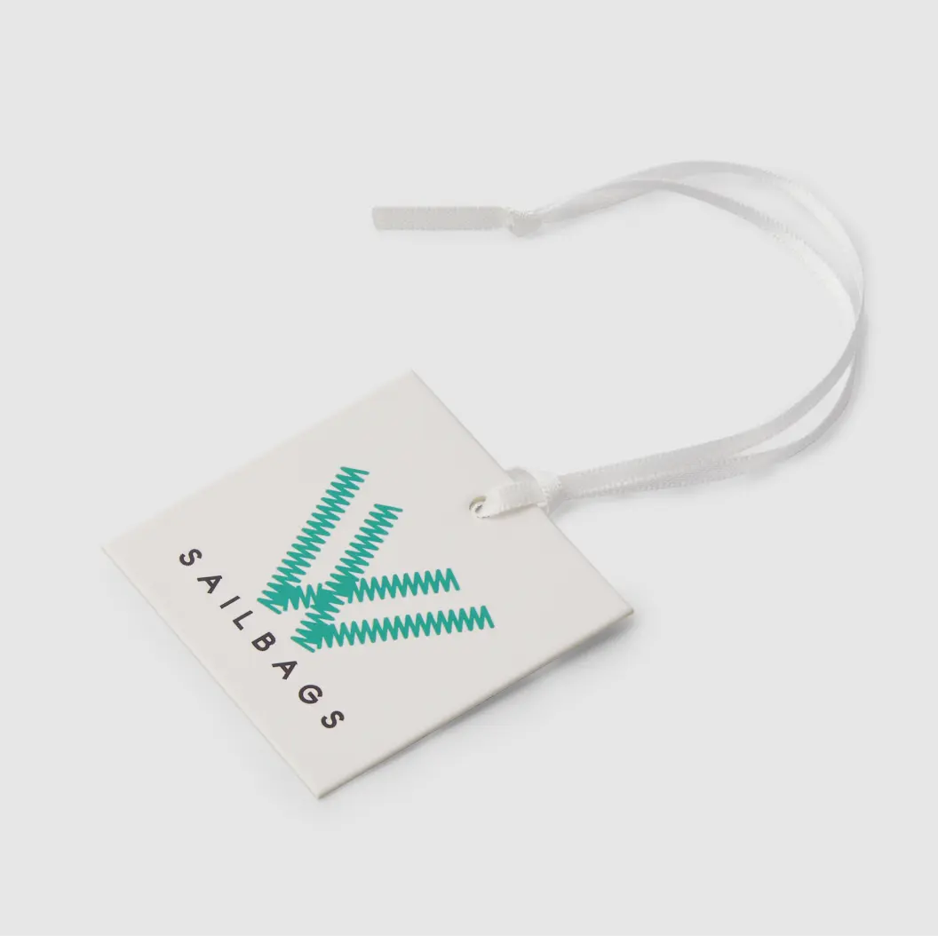 White square hang tag with a green geometric design and “Sail Bags” text, attached to a white string.