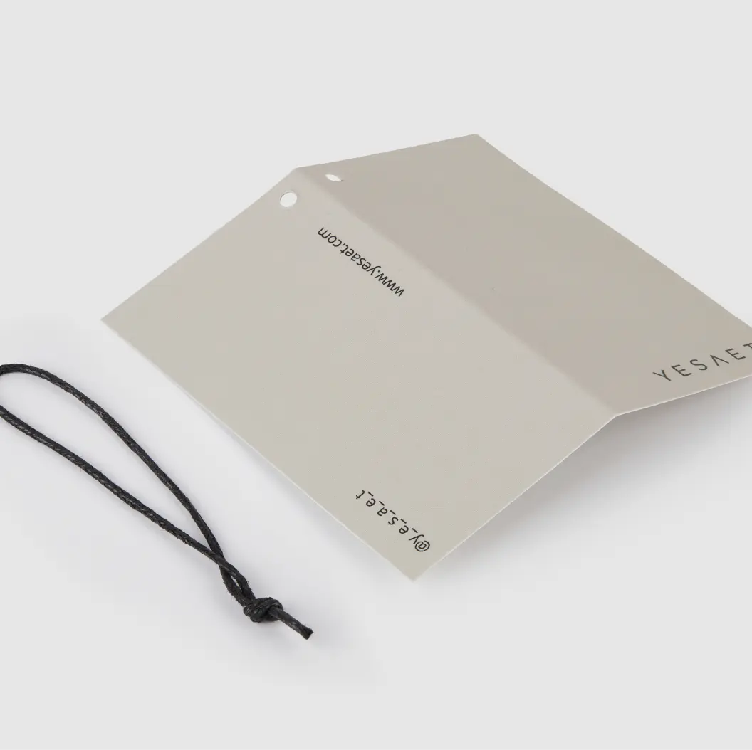 Folded grey hang tag with black string, featuring a simple logo and website information.