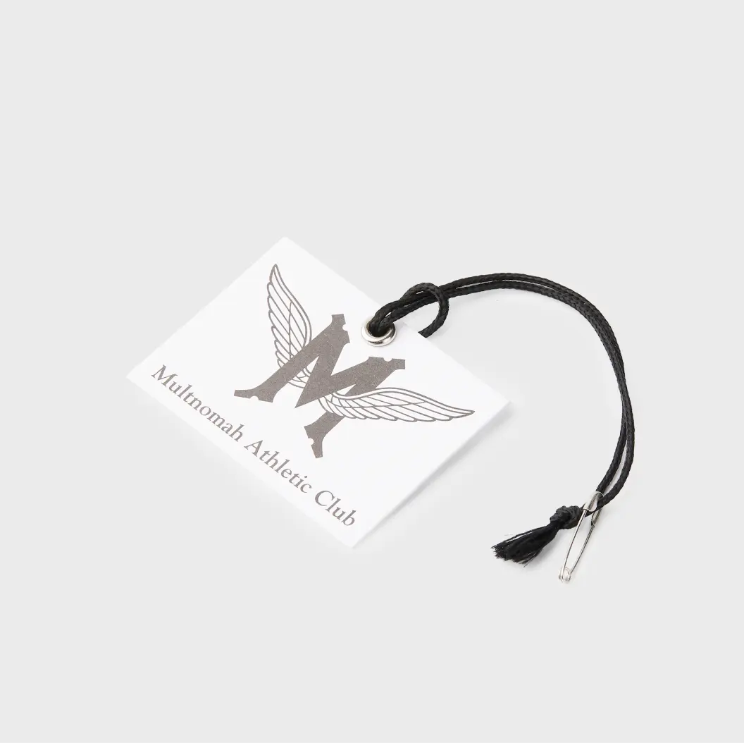 White square hang tag with a winged “M” logo and black string, representing the Multnomah Athletic Club.