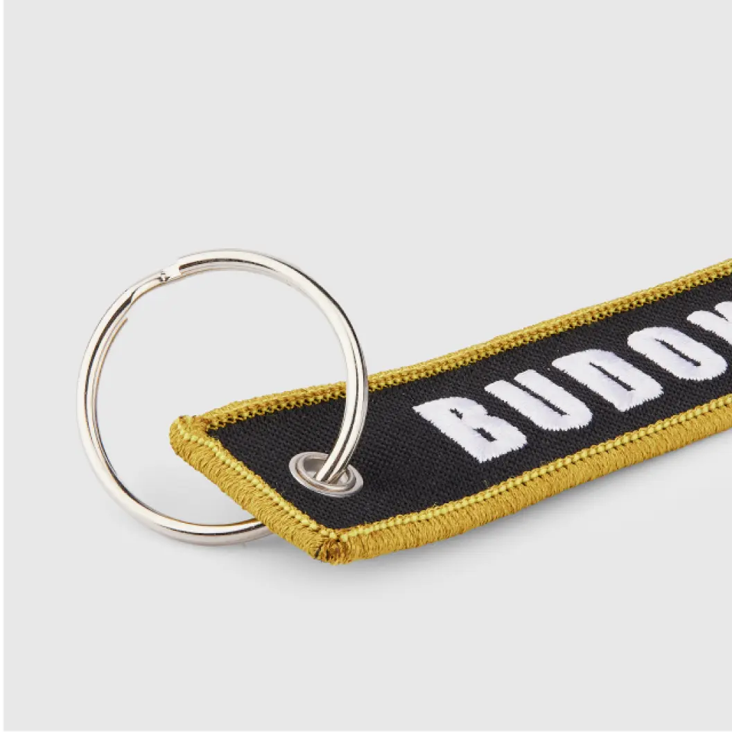 Black embroidered keychain with a gold border and bold white text.