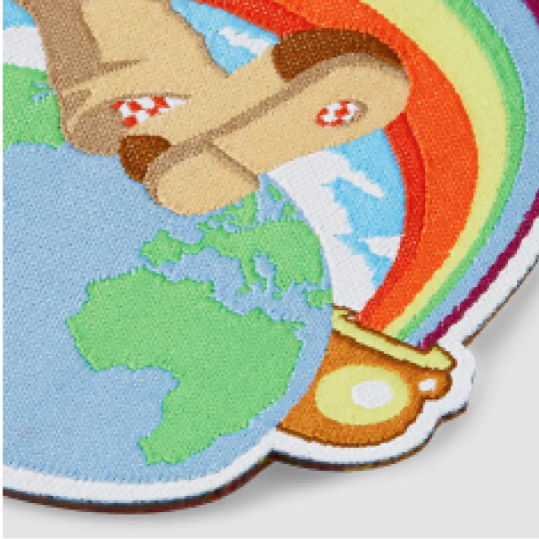 Close-up of woven patch featuring a cartoon-style globe, stepping leg, and rainbow.