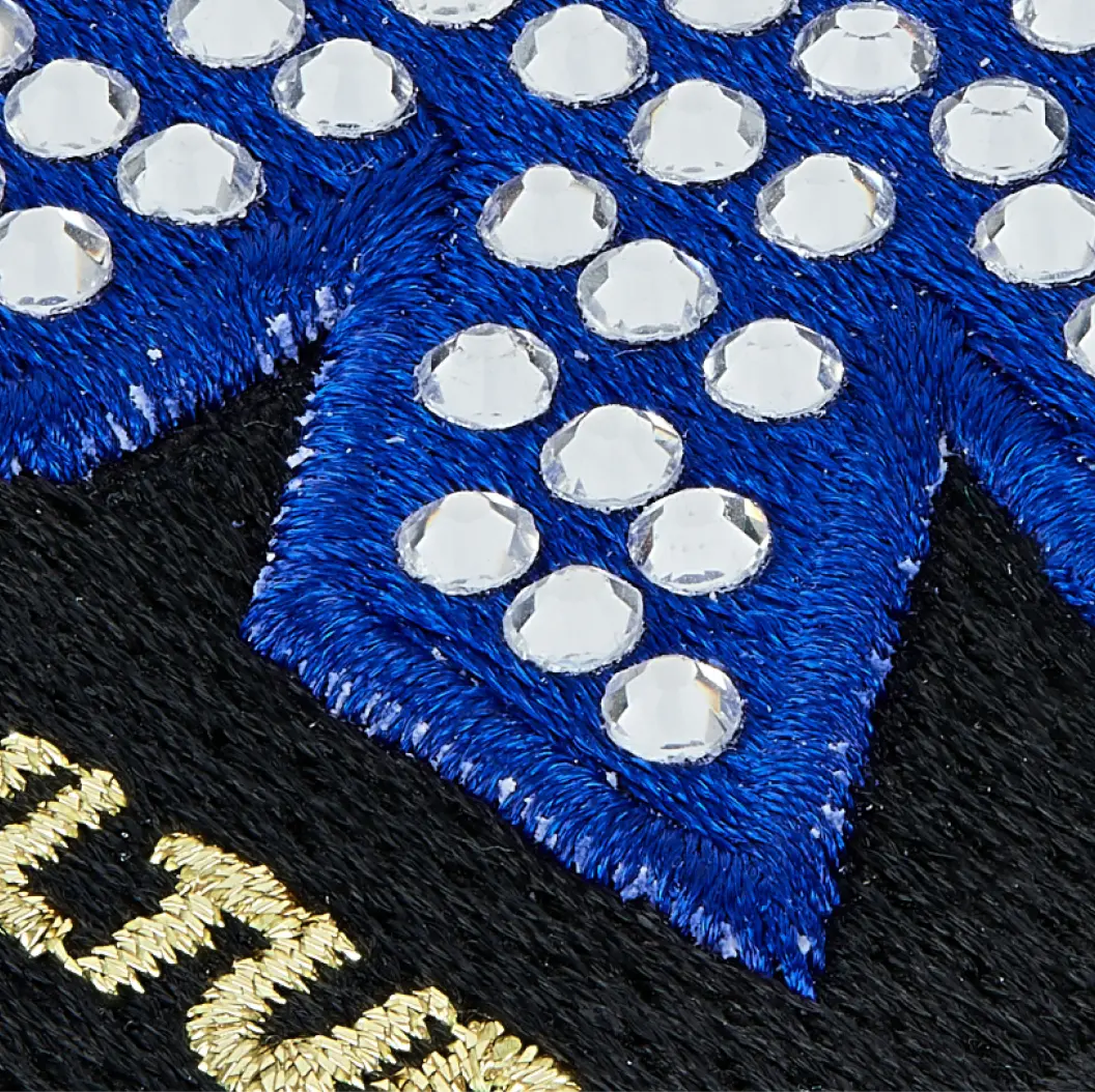 Close-up of an embroidered patch with intricate stitching, adorned with rhinestones for added sparkle and texture.