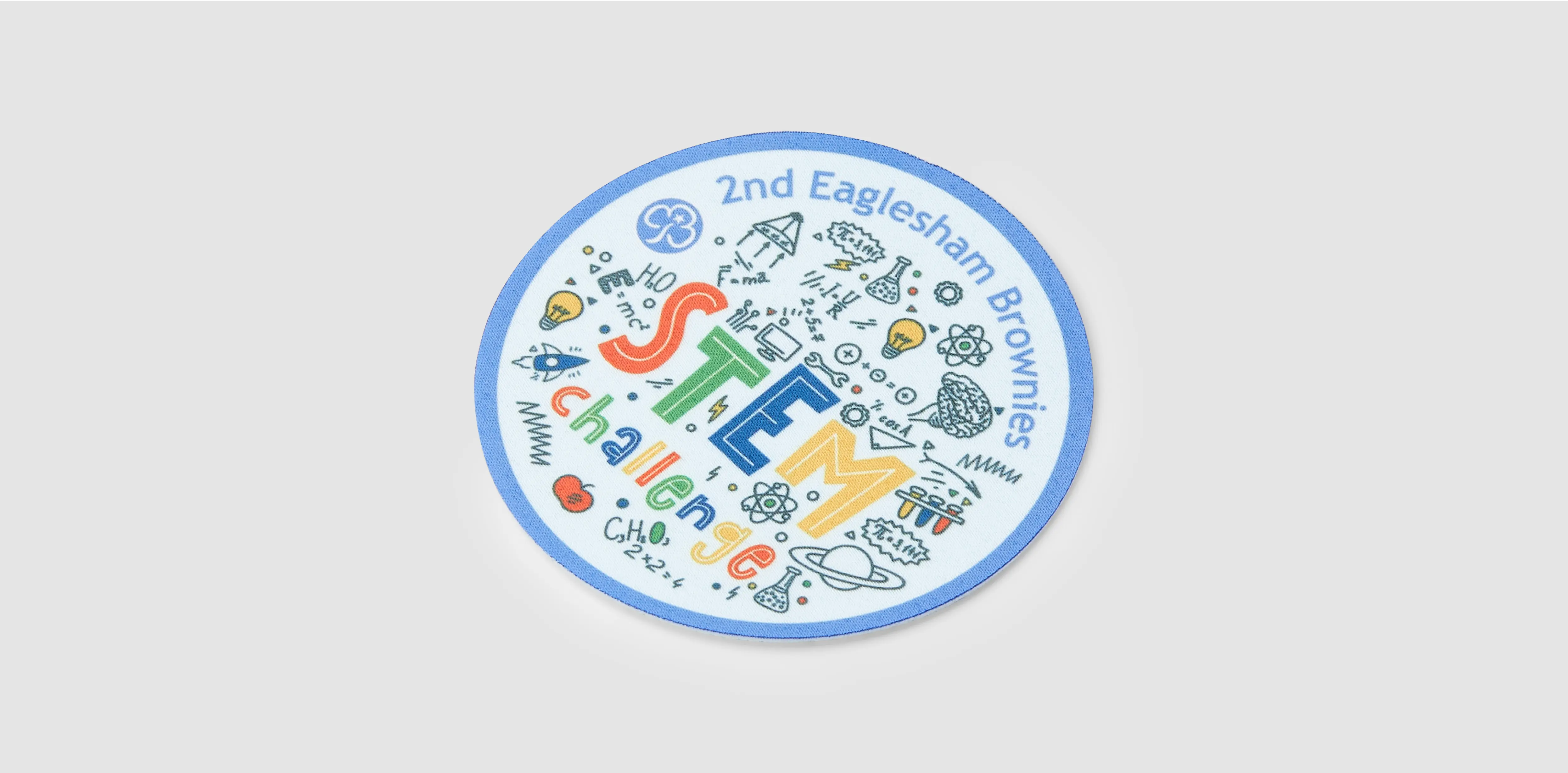 A round patch featuring colorful icons and the text “STEM challenge” in blue, red, and yellow with a light blue border.