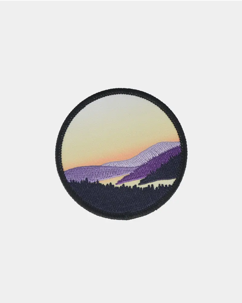 Scenic embroidered patch showing a sunset with purple and black mountains, outlined with a black border