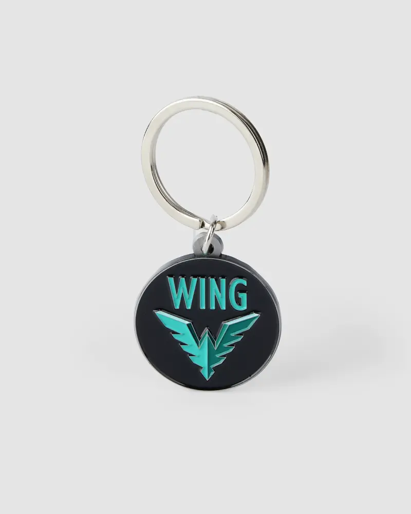 Circular black metal keychain with a turquoise WING logo and shield with wings.