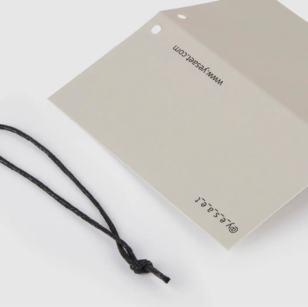 Folded grey hang tag with black string, featuring a simple logo and website information.