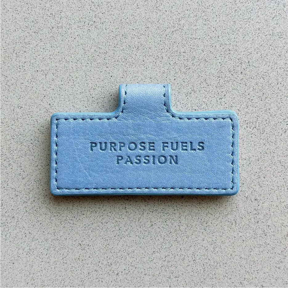 Blue leather label with the text ‘Purpose Fuels Passion’ embossed in the center