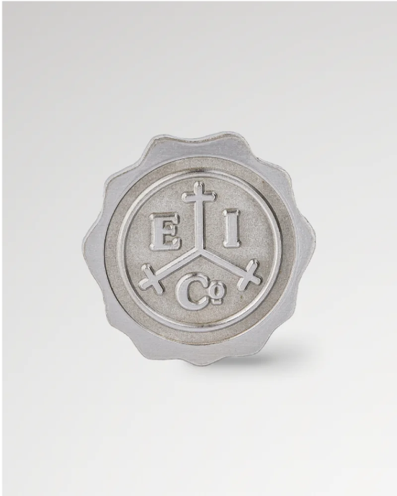 Silver round pin with engraved “E I Co” and a cross design on the surface.