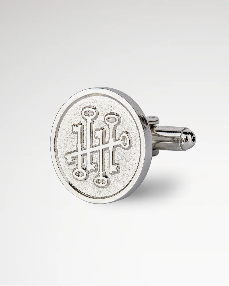 Silver cufflink with key design engraved on the surface.